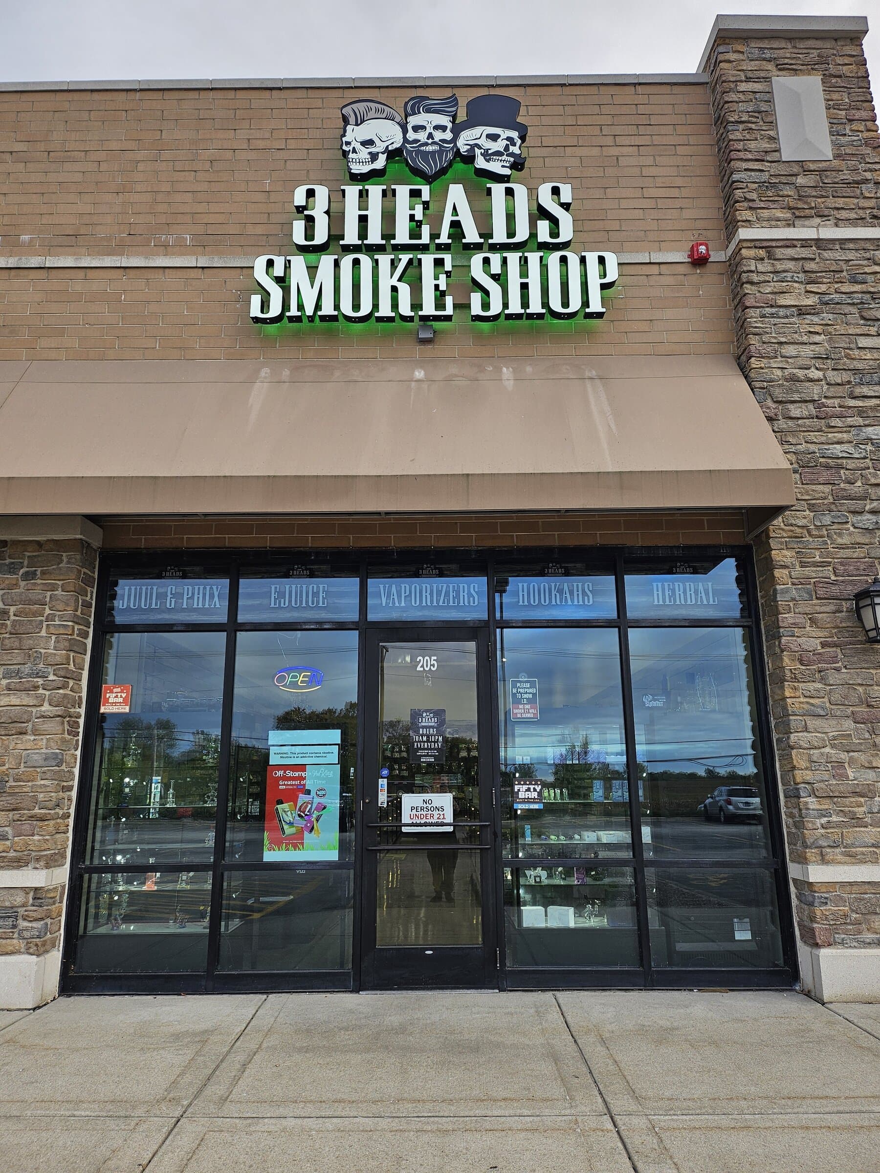 The 3 Heads Smoke Shop storefront in Elgin — the lit three-skull sign above windows marked Juul & Phix, e-juice, vaporizers, hookahs, and herbal